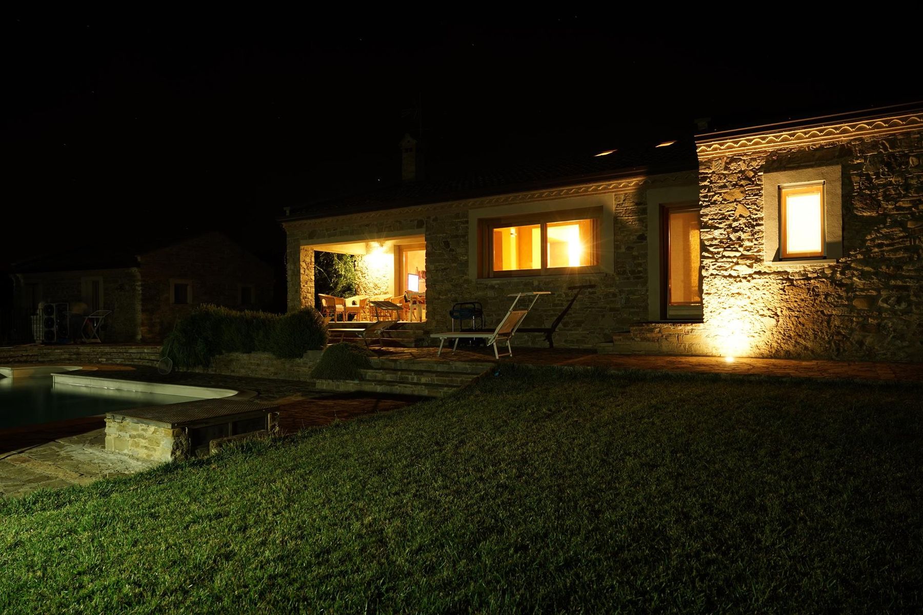 Il casale illuminato di sera, con il porticato e il prato